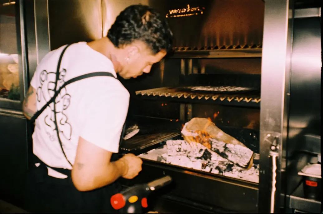 Un cocinero atiende el fuego de la brasa en la cocina a la vista