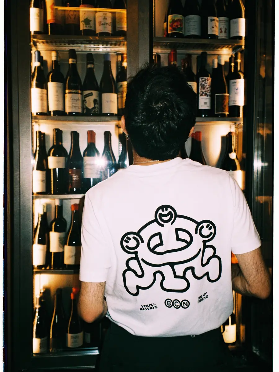 Un camarero de espaldas, con la mascota de Amicks en la camiseta, frente a la nevera de vinos