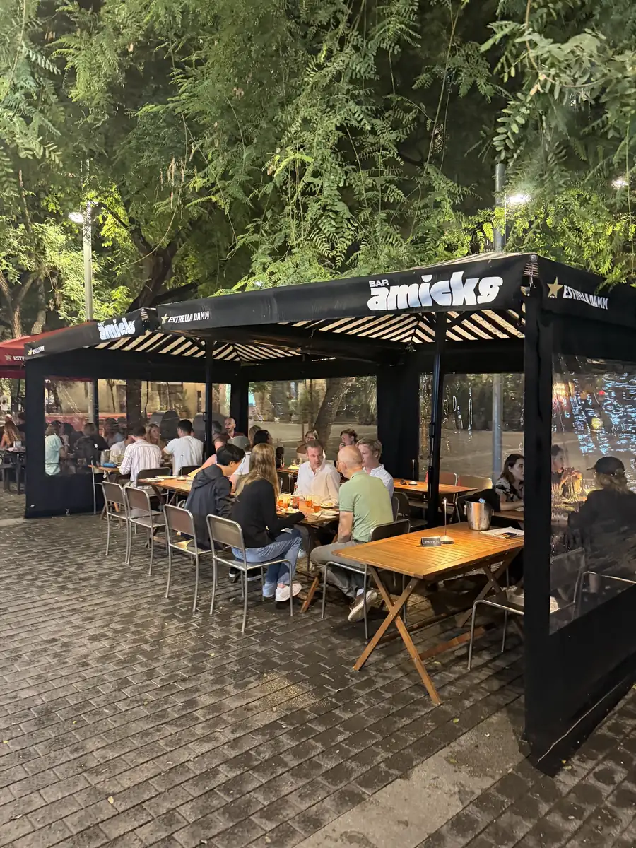 La terraza de Bar Amicks por la noche, con las mesas llenas bajo el toldo