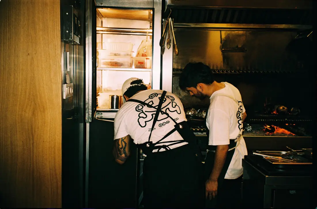 Dos cocineros trabajan en la brasa de la cocina abierta