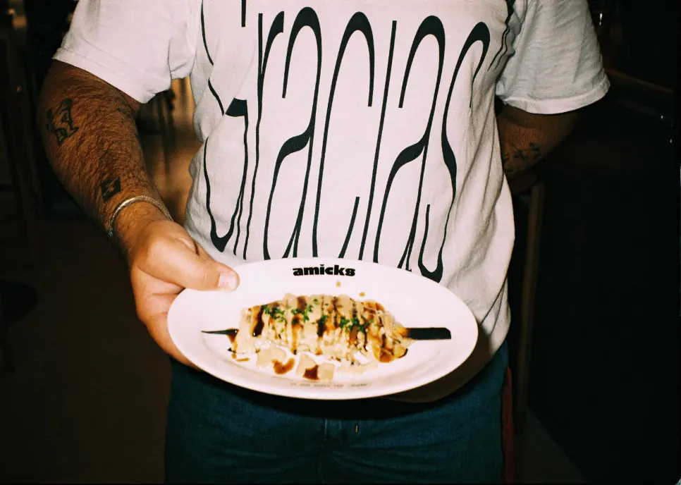 Un camarero con una camiseta que dice Gracias sostiene una brocheta de céleri con el logo de Amicks