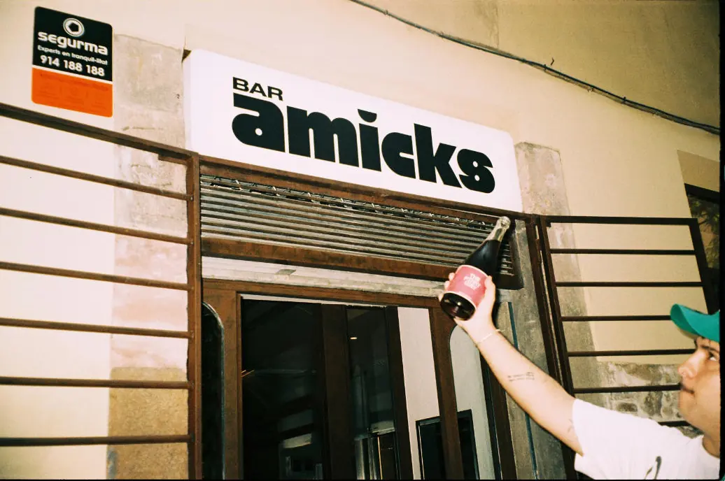 Un camarero cuelga una botella junto al rótulo de Bar Amicks