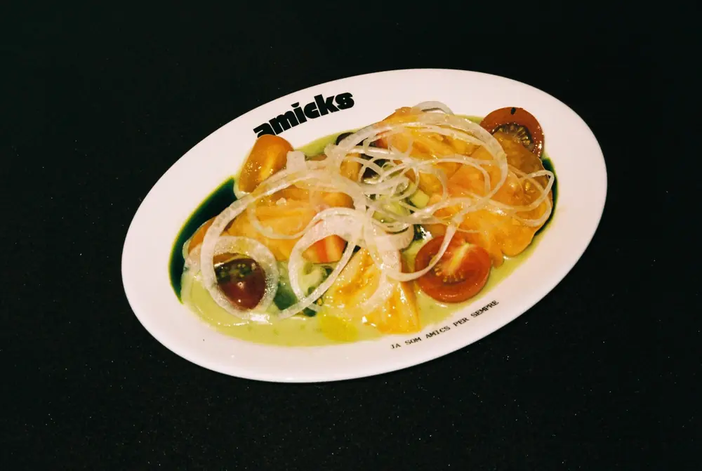 Ensalada de tomates de temporada con cebolla, en un plato con el logo de Amicks